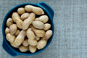 Roasted peanuts in a blue cup, on gray canvas.