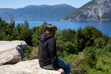 Young girl sitting on a rock look at the lake and mountains. Bariloche, Argentina