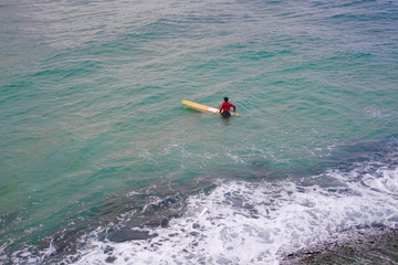 One Surfer man in a red jacket with a yellow surfboard in the azure ocean.