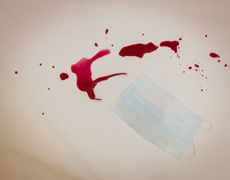 Medical face mask on the white bacground with red liquid (blood) around it. Copy space image. Concept of Medical conditions and industry of medical care.