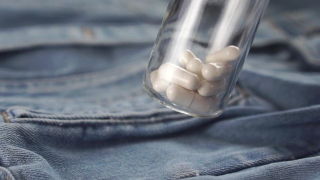 bottle with white capsules shakes over blue denim clothes. Slow motion. Close-up. The concept of the use of stimulants for the treatment of sexual dysfunction