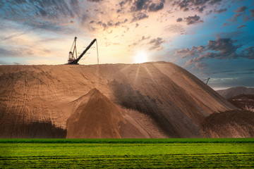 Extracting and mining potassium and magnesium salts.Large excavator machine and Huge mountains of waste ore in the extraction of potassium against the backdrop of a dramatic sunset sky. 