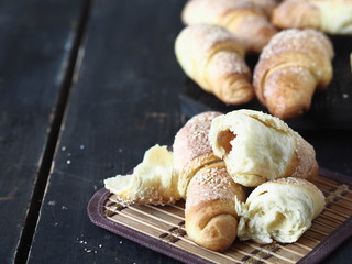 Croissants sprinkled with sesame and sugar on a dark wooden background.Homemade cake.