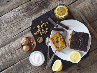 Lemon tea and homemade holiday pumpkin chocolate soft cake, drenched with chocolate on a dark kitchen board with walnuts on a wooden ancient background.View from above.