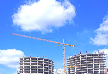 Big construction cranes with a background of a blue sky with fluffy clouds. 