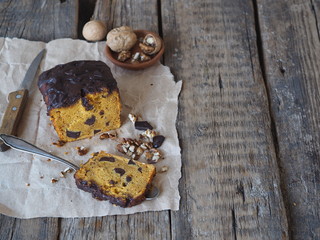 Festive pumpkin chocolate soft muffin, poured with chocolate icing on parchment paper with walnuts on a wooden ancient background.Homemade baking.