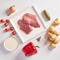 Delivery of packaged food for dinner. meat in plactic bag and vegetables: potatoes, onions, spices, cherry tomatoes, red pepper on white background