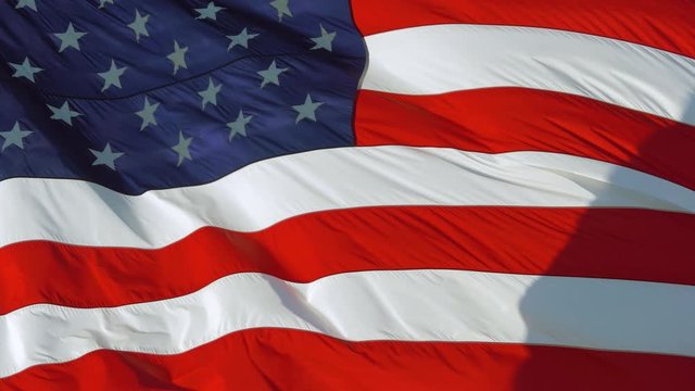 AMERICAN FLAG BACKGROUND: American flag is flying in the wind on a sunny day. Symbol of the Amenrican national holiday. United States flag waving textile fabric textured background, full screen, 4K.