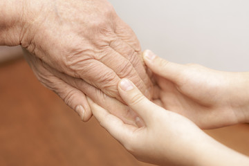 The hands of an old grandmother and a child touch in a handshake for support and help.