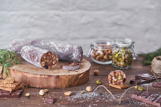Traditional homemade chocolate salami with hazelnuts and pistachios on wooden board placed on table with ingredients and green spruce branches