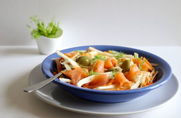 Concetto di cibo. Insalata fresca con salmone affumicato, finocchio, carote, olive ed erbe sul piatto blu. Sfondo bianco. Vista dall'alto.