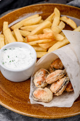 Mussel and french fries on a brown plate on a dark concrete background, decorated with fresh vegetables