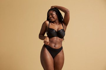 Curvy beautiful African American woman with braids in lingerie with closed eyes against yellow background