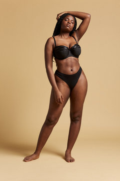Curvy beautiful African American woman with braids in lingerie with closed eyes against yellow background