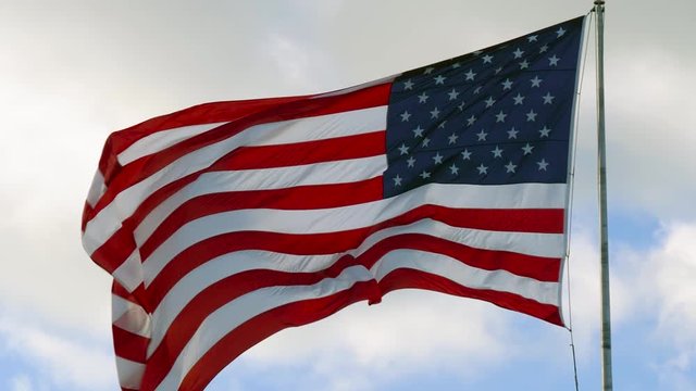 American USA flag on a flagpole waving in the wind. Slow Motion USA Flag Waving United States of America Flag Flying in HD Video. Close up of American flag waving.