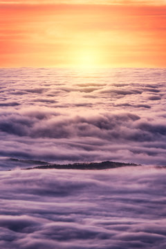 From above of black peaks of powerful mountains among soft white thick clouds at sunrise