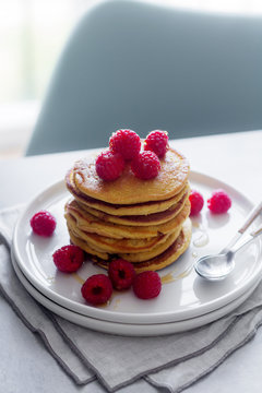 Stack of tasty pancakes with ripe raspberries placed on plate near spoons on gray background