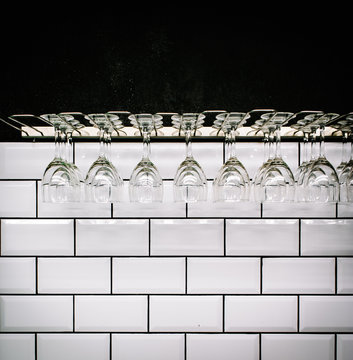 Row of clean polished wineglasses hanging against white tiled wall in vintage bar