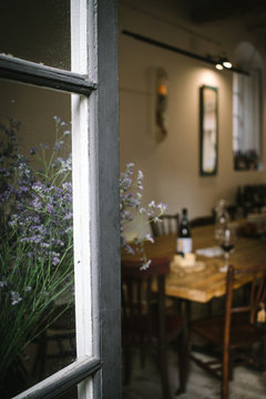 Fragment of interior of rustic restaurant with wooden table served with wine and cheese seen from open window with flowers