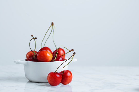 Fresh ripe red cherry with stalks in white ceramic pot placed on marble table against white wall