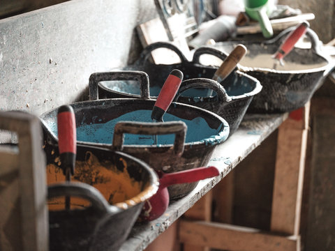 Side view from above of black containers with blue white yellow glazes and tools on wooden shelf in factory