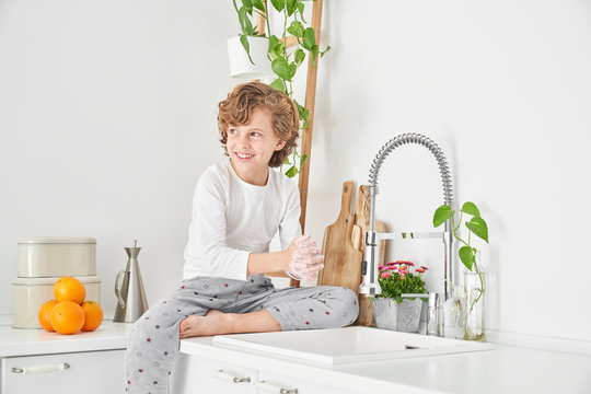 Blond child washing his hands in the kitchen sink to prevent any infection