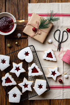Top view of tasty homemade cookies of various shapes with red berry jam and white sugar powder placed on wooden table with utensils and decorative elements for Christmas celebration