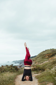 Flexible woman in sporty clothing practicing yoga in Inverted Eagle Pose garudasana on empty path among green grass on hill