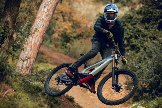 Unrecognizable man in helmet, gloves and protection glasses jumping doing whip trick downhill during mountain biking practice in wood forest