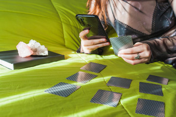 Close-up of a woman doing a tarot card reading on her bed while looking at her smartphone