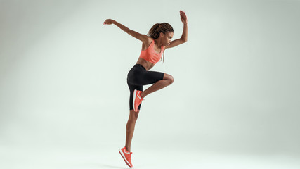 Never stop. Full length of young african woman with perfect body in sports clothing jumping in studio against grey background