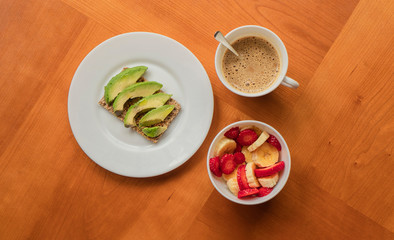 Avocado toast, cup of coffee and strawberry-banana mix in a wooden table