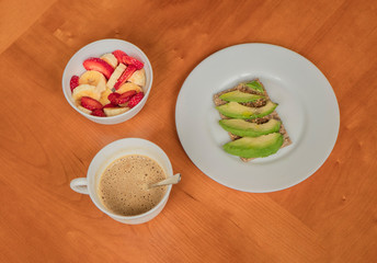 Avocado toast, cup of coffee and strawberry-banana mix in a wooden table