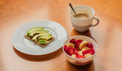 Avocado toast, cup of coffee and strawberry-banana mix in a wooden table
