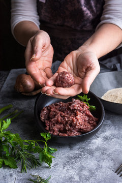 From above unrecognizable person wearing apron showing meatball to camera over bowls with minced meat during lunch preparation