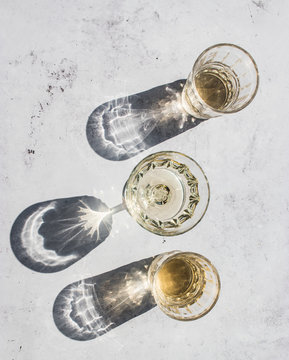 Top view composition of various glasses with alcohol drinks in sunlight leaving shadows and lights on marble surface