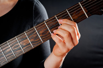Fototapeta na wymiar Seven-string electric guitar made of dark wood and human hands, shot on a dark background. Background for musical instruments and musicians.