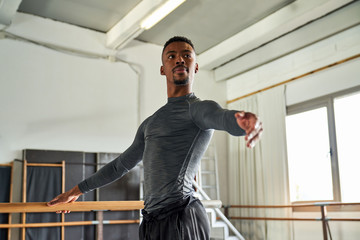 Professional ballet dancer looking away while training in a modern studio using wooden handrail