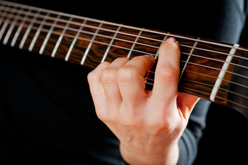 Seven-string electric guitar made of dark wood and human hands, shot on a dark background....