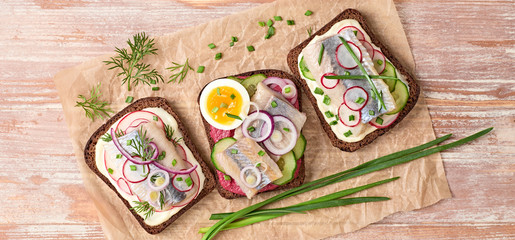 Fototapeta na wymiar Smorrebrod traditional Danish sandwiches fish, radish, mayonnaise. Open sandwich with rye bread, herring on wooden background, top view. Tasty fish smorrebrod. Flat lay