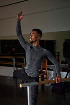 Professional ballet dancer looking away with leg up while training in a modern studio using wooden handrail