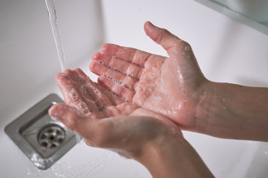 From above top view cropped unrecognizable child boy washing hands under running water carefully in modern bathroom at home