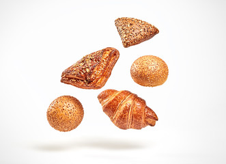 Croissant bun brioche cake flying in air. Fresh baked cookie with sesame, sunflower seed falling on...