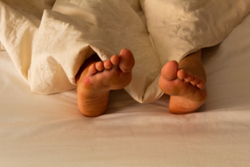 Legs of a woman lying down, covered with white sheets, concept of rest, sleep and relax