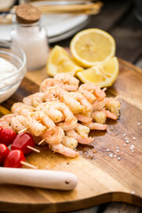 Shrimps prepared for grilling with lemon, salt, dip and tomato on a wooden board, natural light