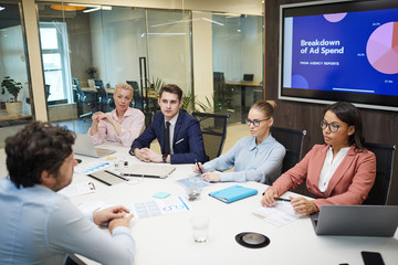 Business people sitting at the table in board room and discussing new project with presentation on the screen in the background