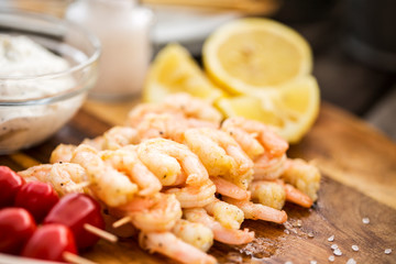 Shrimps prepared for grilling with lemon, salt, dip and tomato on a wooden board, natural light