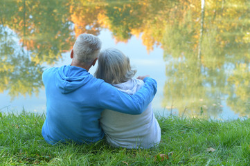 Happy senior woman and man in park sitting by pond
