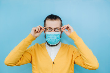 A young man in a medical mask on a blue background. A man in a yellow cardigan shows a hand gesture OK. We're going to beat coronavirus. The COVID-2019 epidemic. Positive boy.