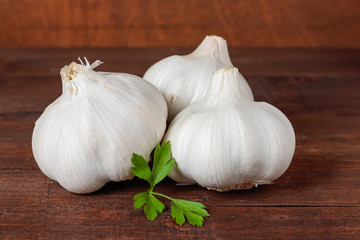 three garlic heads and parsley on a wooden table